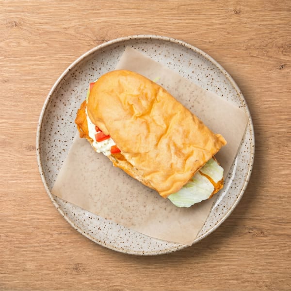 A fried fish sandwich with lettuce, tomato, and tartar sauce on a speckled plate.