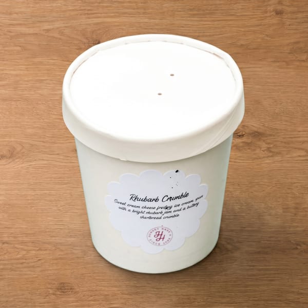 A white pint of "Rhubarb Crumble" ice cream with a decorative label on a wooden surface.