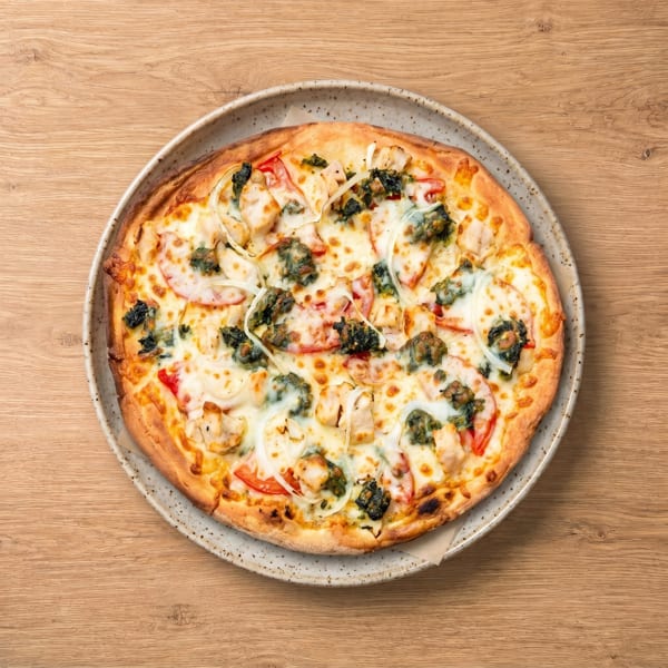 Overhead view of a whole pizza with chicken, tomatoes, onions, and pesto on a speckled plate.