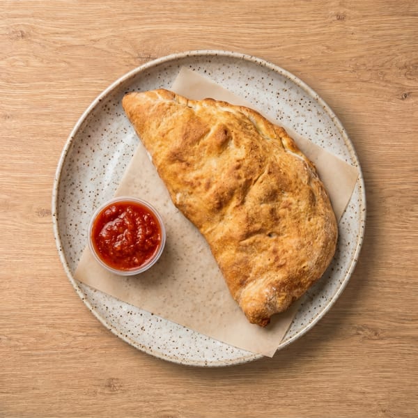 Golden-brown calzone with a side of red marinara sauce on a speckled plate.