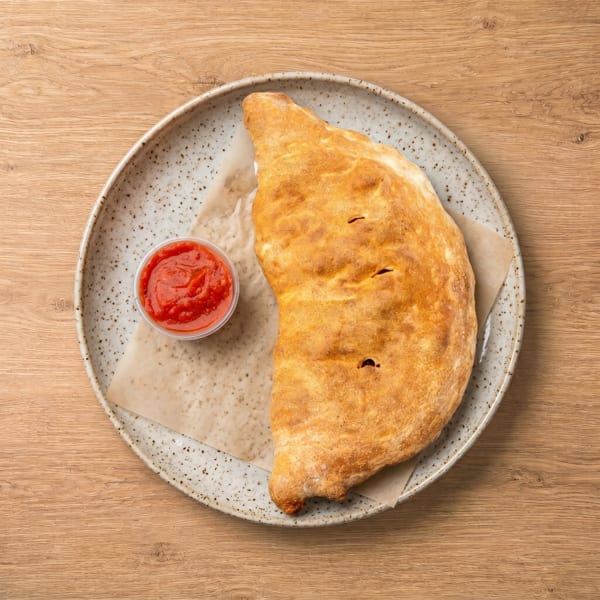 Golden-brown calzone with a side of red marinara sauce on a speckled plate.