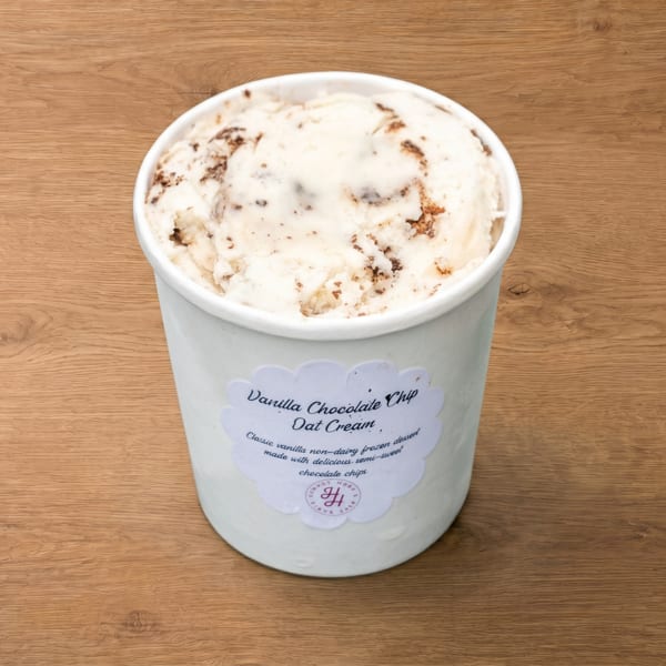 A white pint of Vanilla Chocolate Chip Oat Cream, a non-dairy frozen dessert, on a wooden surface.