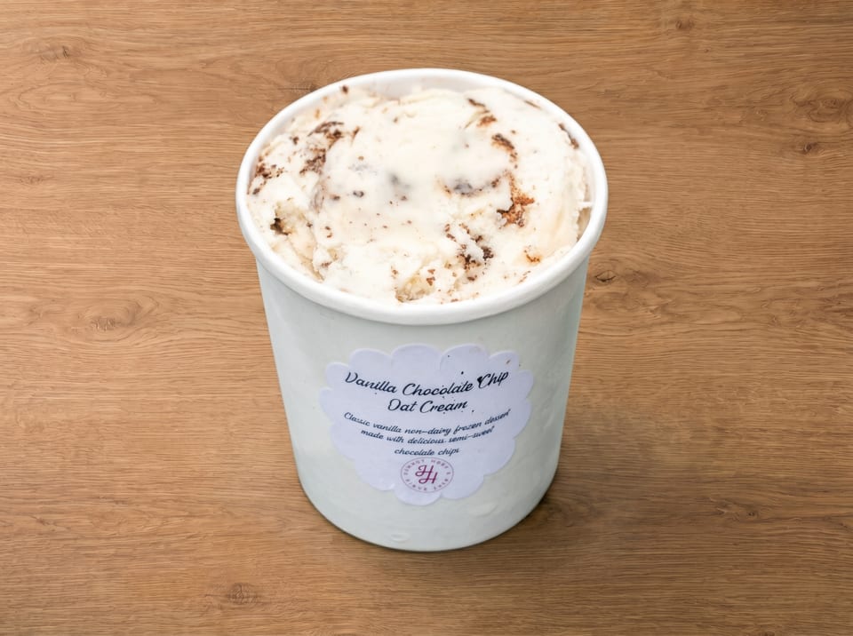 A white pint of Vanilla Chocolate Chip Oat Cream, a non-dairy frozen dessert, on a wooden surface.