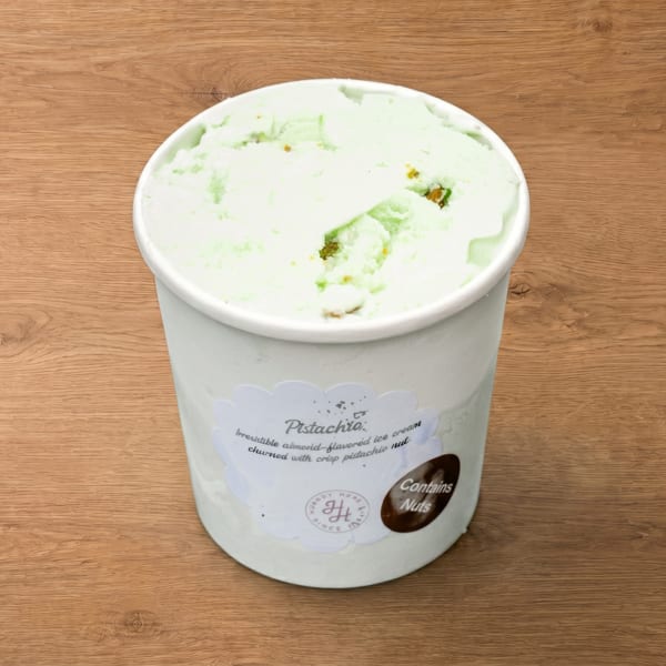 A white tub of pistachio ice cream with a label on a wooden surface.