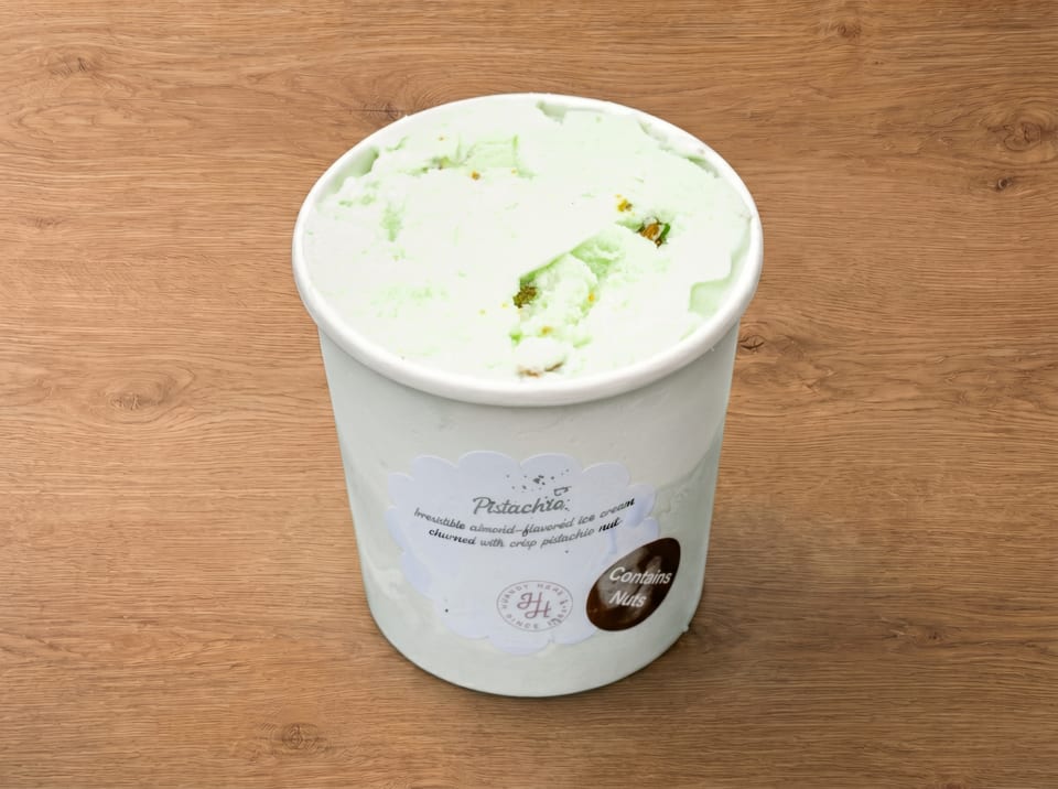 A white tub of pistachio ice cream with a label on a wooden surface.